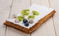 Belgian waffle with cream, kiwi and blueberries. On a light wooden background