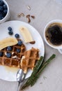 Belgian waffles with honey, blueberries, banana and almonds with a cup of fresh coffee