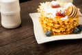 Belgian waffles with raspberries and sieving sugar powder and honey served with jug of milk on a white table