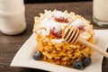 Belgian waffles with raspberries and sieving sugar powder and honey served with jug of milk on a white table