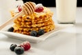 Belgian waffles with raspberries and sieving sugar powder and honey served with jug of milk on a white table