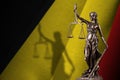 Belgium flag with statue of lady justice and judicial scales in dark room. Concept of judgement and punishment