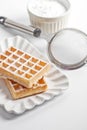 Belgium wafers with sugar powder on ceramic plate and strainer on white table