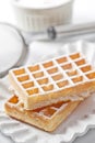 Belgium wafers with sugar powder on ceramic plate and strainer on white table