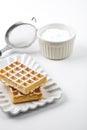 Belgium waffers with sugar powder on ceramic plate and strainer on white table