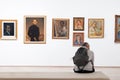 02.01.2023 Belgrad.Gallery Back view of man with backpack sitting on bench and watching at frames with art picture. Copy Royalty Free Stock Photo