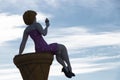 Giant sculpture of an attractive woman sitting on a cone and eating ice cream against the dusk sky