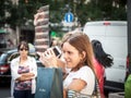 Two girls standing and observing developped film negative from analog photography in the streets while holding a smartphone.