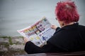 Old woman sitting on a bench reading the serbian tabloid newspaper Informer with governmental propaganda for the SNS party