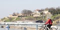 Young men wearing protective mask cycling over city bridge with Kalemegdan fortress in the background