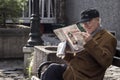 Old Man, happy, sitting on a bench, reading a Serbian newspaper whilebeing relaxed in a street of the center of Belgrade