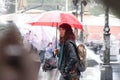 Blurry young woman walking under the red umbrella on rainy and crowd city street
