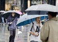 Young woman walking in a hurry under umbrella while talking on a mobile phone on a rainy and crowd city street