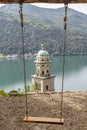 The bell tower of the church of Santa Maria del Sasso in Morcote, Switzerland, framed by the ropes of a high swing