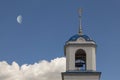 The bell tower of the Orthodox Church against the backdrop of the blue sky with the Moon visible