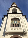 The bell tower of the Orthodox church with the faces of saints on the facade, the view from up against the blue sky