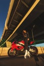 Biker Woman on motorcycle against bridge. Young brutal cute girl wear black leather jacket and sunglasses Royalty Free Stock Photo