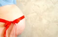 Belly of a pregnant girl tied with a gift red ribbon with a bow on a gray wall background Royalty Free Stock Photo