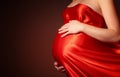 Belly of pregnant woman in red silk dress billowing