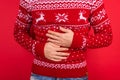 Bellyache concept. Close up photo of men in red winter sweater with deers holding his stomach on red background