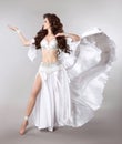 Bellydance. Beautiful belly dancer woman in white shining costume with blowing fabric. Long healthy curly hair. arabian