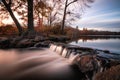 Smooth milky stream of water cascading down rocks from a glassy still lake surrounded by fall foliage.