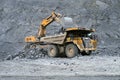 Excavator Liebherr loads ore in a dump truck Caterpillar in the background of a quarry.