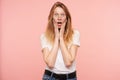 Bemused young pretty redhead female with casual hairstyle rounding her green eyes while looking amazedly at camera and holding