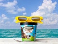 Ben Jerry`s Chocolate Fudge Brownie Ice Cream on white wooden table against tropical turquoise sea water and sky background
