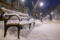 A bench covered with snow on a night boulevard in the city in the light of lanterns. Winter city landscape Royalty Free Stock Photo
