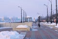 A bench with a flower bed in winter, filled with a snowdrift. Rotunda and lighthouse on the embankment. Blurred in the Royalty Free Stock Photo