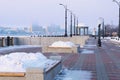 A bench with a flower bed in winter, filled with a snowdrift. Rotunda and lighthouse on the embankment. Blurred in the Royalty Free Stock Photo