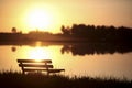 Bench in front of lake in city park with sunset and blurred background, Royalty Free Stock Photo