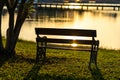 A bench on grass  near tree and water in the parks at sunset Royalty Free Stock Photo