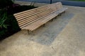 wooden long park bench with curved backrest anatomical wooden cladding made of light wood on the ground light beige gravel, which