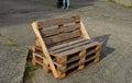 Bench made of returnable pallets for goods. it has a back and seat made of wooden planks. stands on a concrete surface in the park