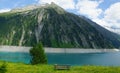 Bench and mountain lake and glaciers and clouds and grasses and yellow flowers and fresh water in the Alps for relaxation