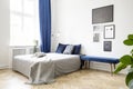 Bench next to bed with grey blanket in bright bedroom interior with posters and blue drapes. Real photo Royalty Free Stock Photo