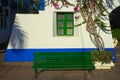 Bench next to a tree growing in front of a white and blue building with green window frames Royalty Free Stock Photo