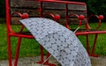 Bench in a park of red color with an umbrella resting near it on a rainy day.