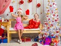 On the bench sits a girl in a cap and mittens of Santa Claus, the other girl with a laugh comes out of the bag Royalty Free Stock Photo