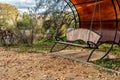 The bench swings kind of sideways brown-colored wooden, chained metallic spring-circle grass