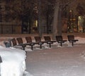 Benches Covered in Snow near Trees and Yellow Building in Winter Royalty Free Stock Photo