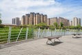 Benches on plank-paved footbridge over lake in modern city of sunny summer