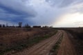 A bend in a country road in an evening field. Twilight landscape. Dramatic cloudy sky Royalty Free Stock Photo