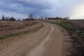 A bend in a country road in an evening field. Twilight landscape. Dramatic cloudy sky Royalty Free Stock Photo