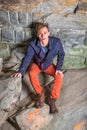 A young guy is standing in a cave of rocks, looking up, hair messed, distressful