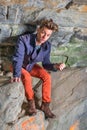 A young guy is standing in a cave of rocks, looking up, hair messed, distressful