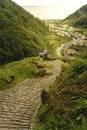 Bending yellow stone pavement pathway descending to the river. Adult couple standing and looking for the sun rays over a tiny vill Royalty Free Stock Photo