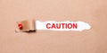 Beneath the torn strip of kraft paper attached with a red button is a white paper labeled CAUTION